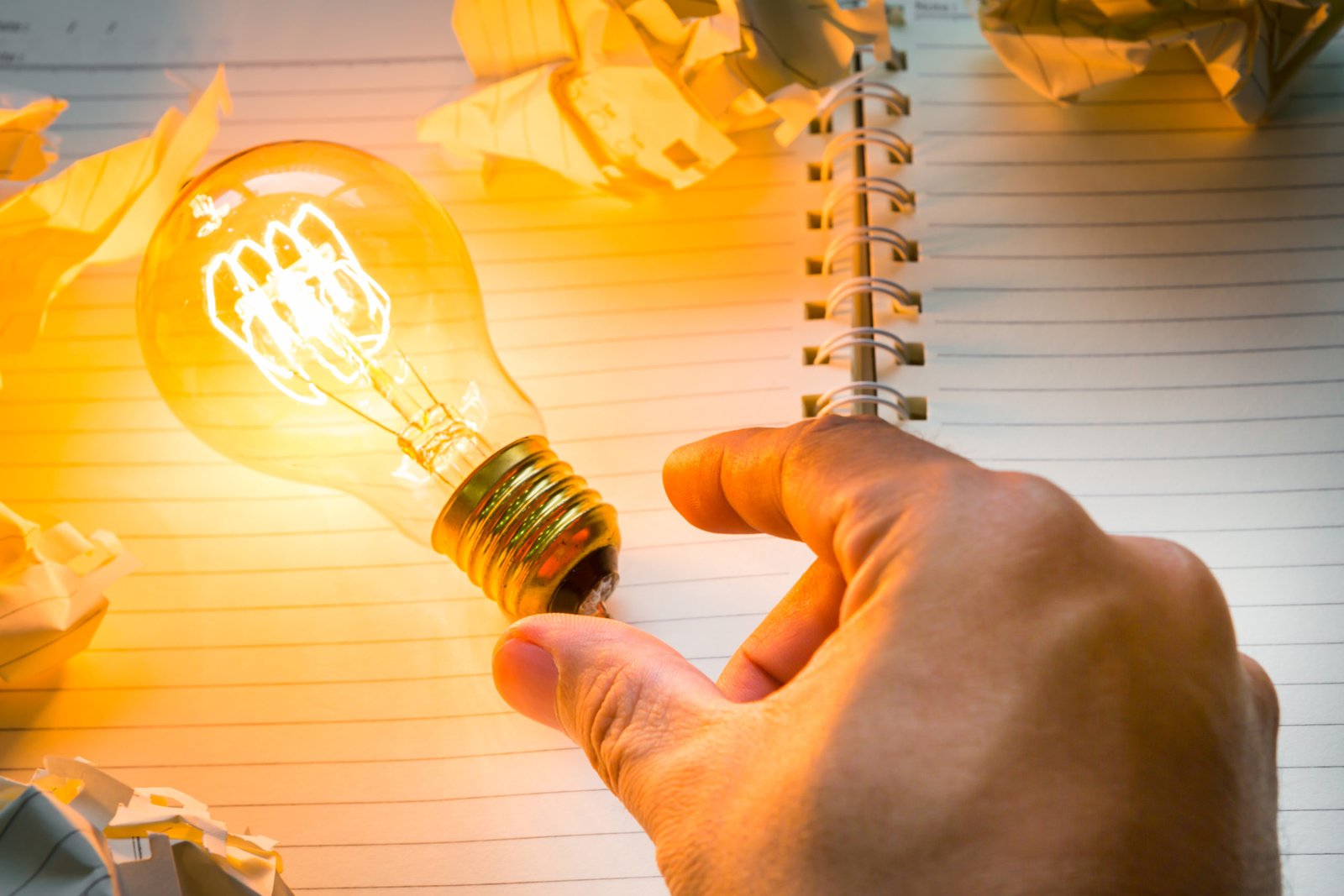 Hand pick light bulb over Note book on wood table